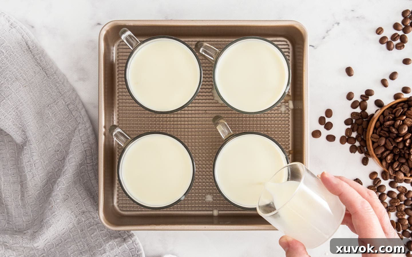 A delicate stream of "crema" being poured slowly over the top of set coffee panna cottas in glasses.