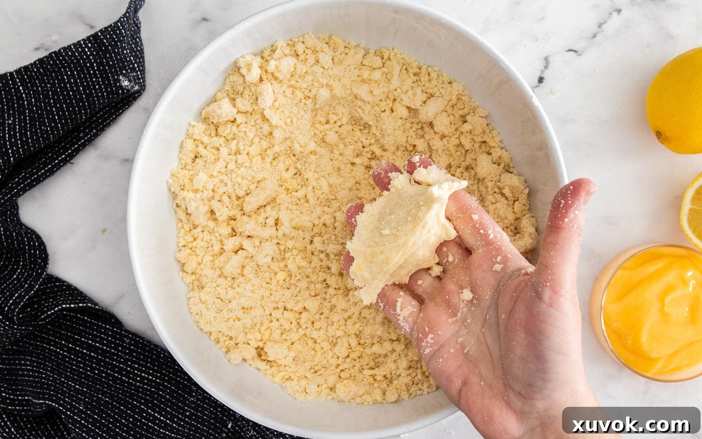 The flour mixture after the melted butter is added with a hand holding a clump of it.