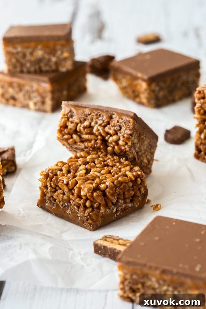 A batch of Snickers crispy cake slices sitting on a sheet of white baking paper, ready to be enjoyed.