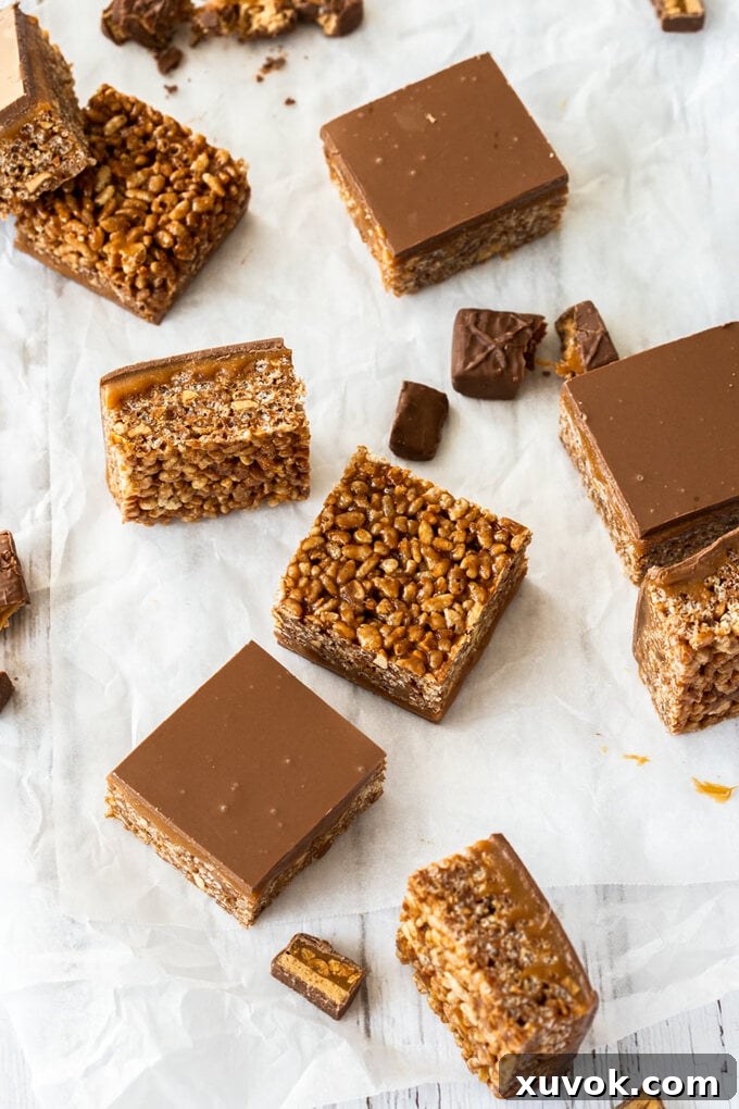 Three decadent chocolate rice krispies treats with caramel and chocolate topping, displayed beautifully on a sheet of baking paper.