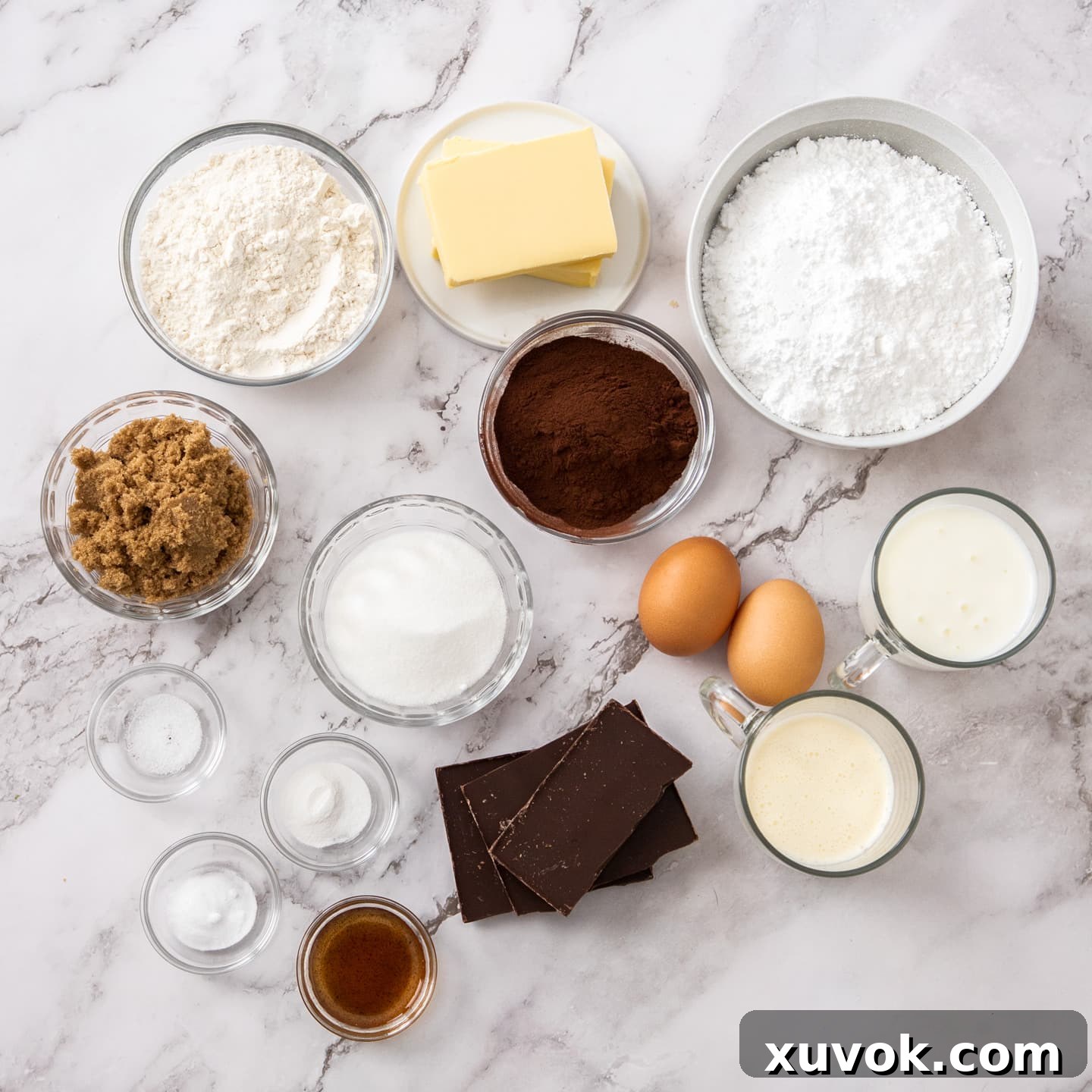 A beautiful arrangement of fresh ingredients for chocolate fudge cupcakes on a pristine marble surface, ready for baking.