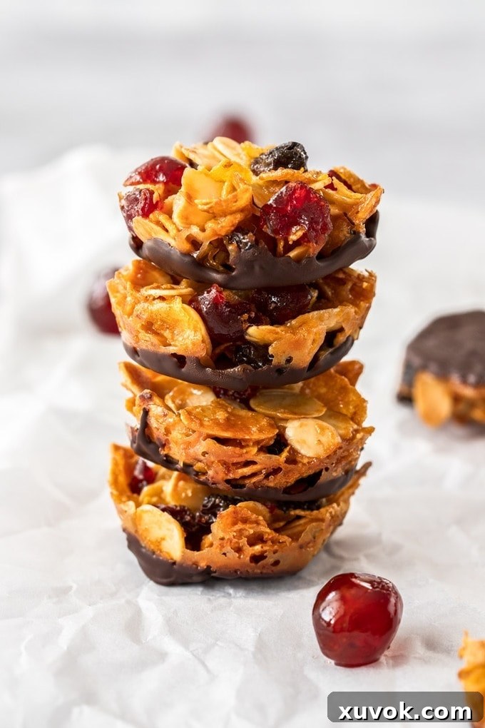 A stack of four golden Florentine biscuits, each with a chocolate base and a vibrant glace cherry on top, resting on baking paper.
