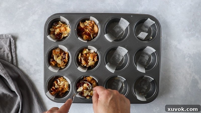 Spoonfuls of Florentine biscuit mixture being carefully placed into a prepared muffin tray before baking.
