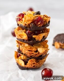 A stack of 4 florentines biscuits with a glace cherry in front, on a sheet of baking paper