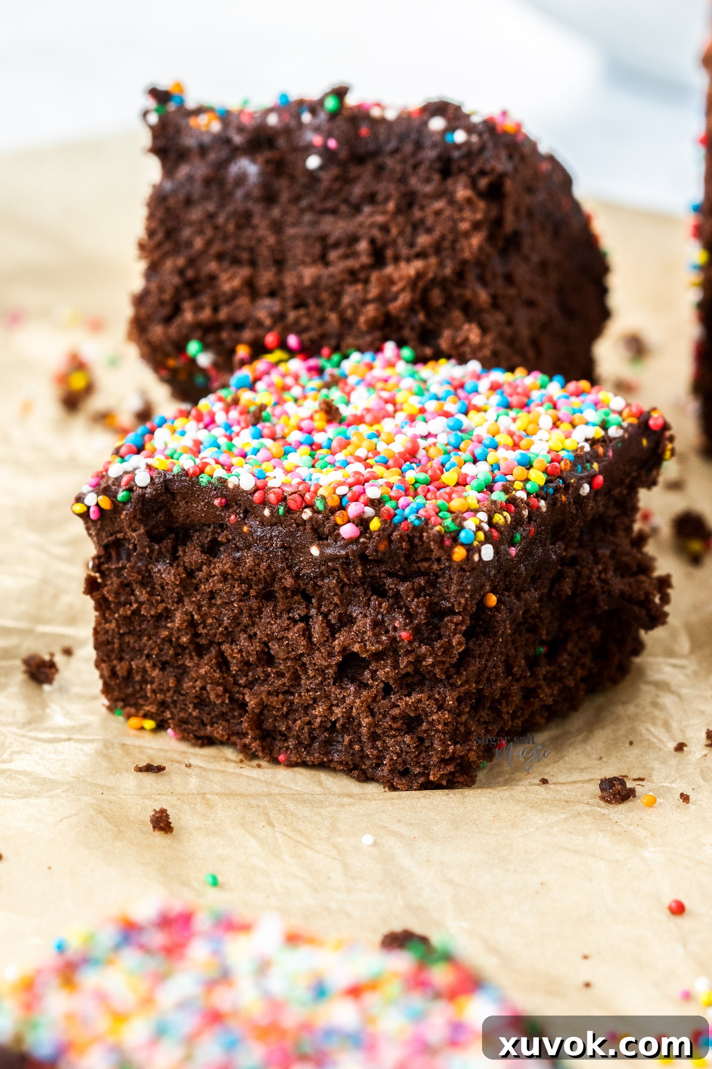 A perfectly square slice of moist chocolate cake, resting gently on a piece of parchment paper.