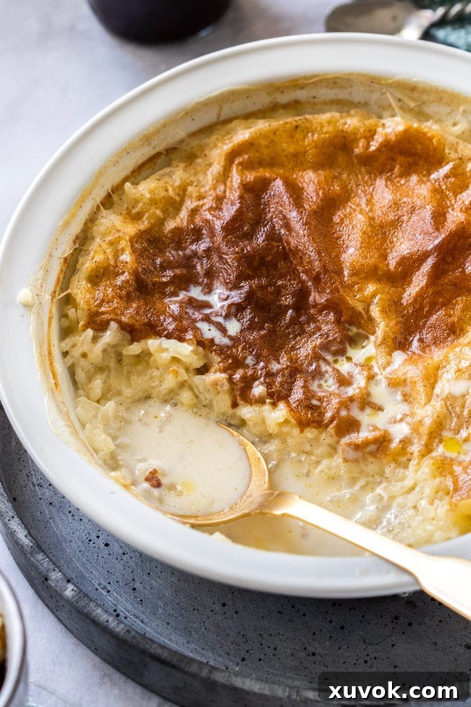 Close up view of a pie dish filled with rice pudding with a gold spoon in it.