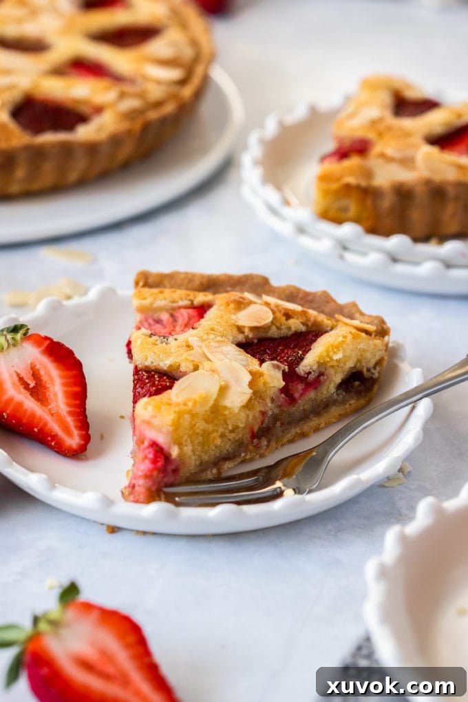 A slice of strawberry tart on a white plate with a fork sitting next to it. More slices in the background