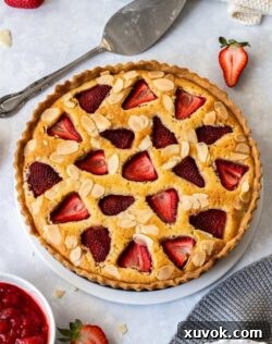 Birdseye view of a baked tart filled with fresh strawberries on a white plate. Some strawberries and dessert plates surround it.