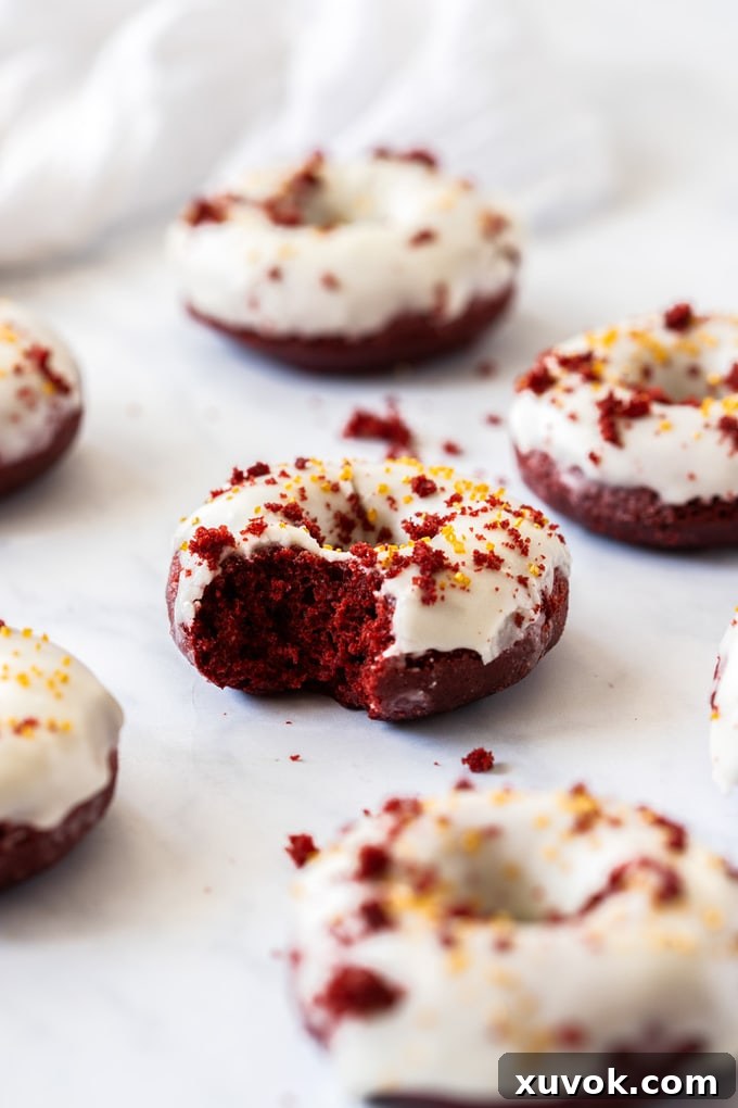 A red velvet donut with a bite taken out of it, showing its soft interior and white glaze