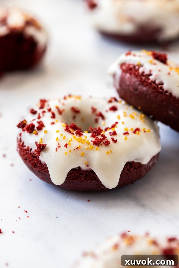 A closeup of a red velvet donut with white icing with another leaning on top of it, showing intricate glaze detail