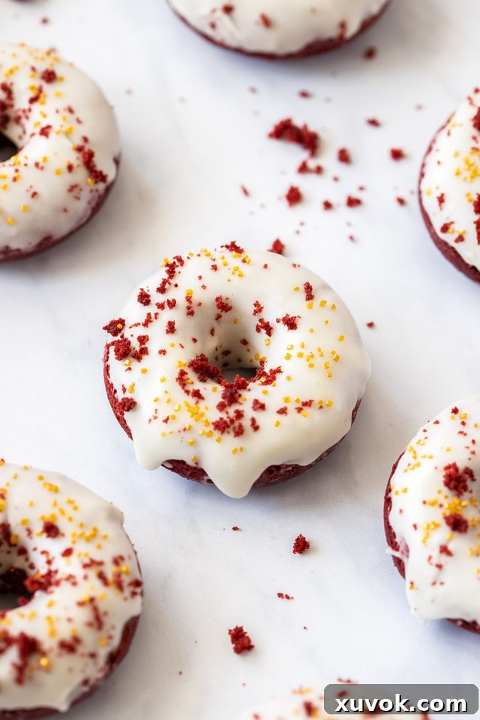 A birdseye view of a donut with white icing and red velvet crumbs, surrounded by more red velvet donuts on a cooling rack