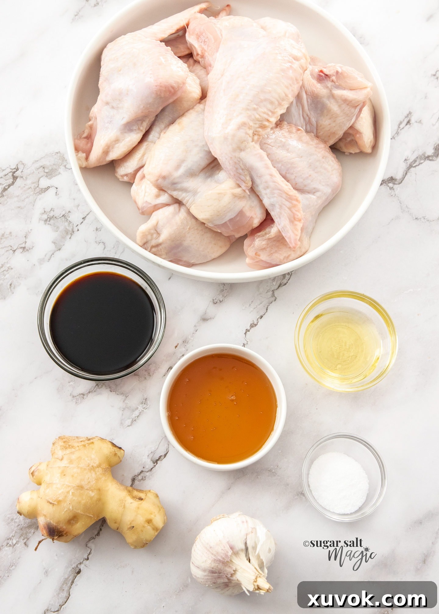 A selection of fresh ingredients laid out on a marble bench top, including chicken wings, honey, soy sauce, ginger, garlic, and baking powder.