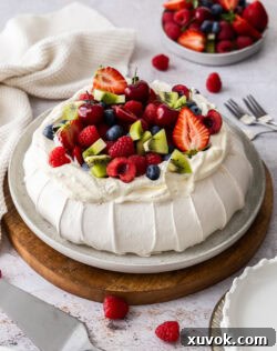 A whole pavlova on a plate, topped with plenty of fresh fruit.