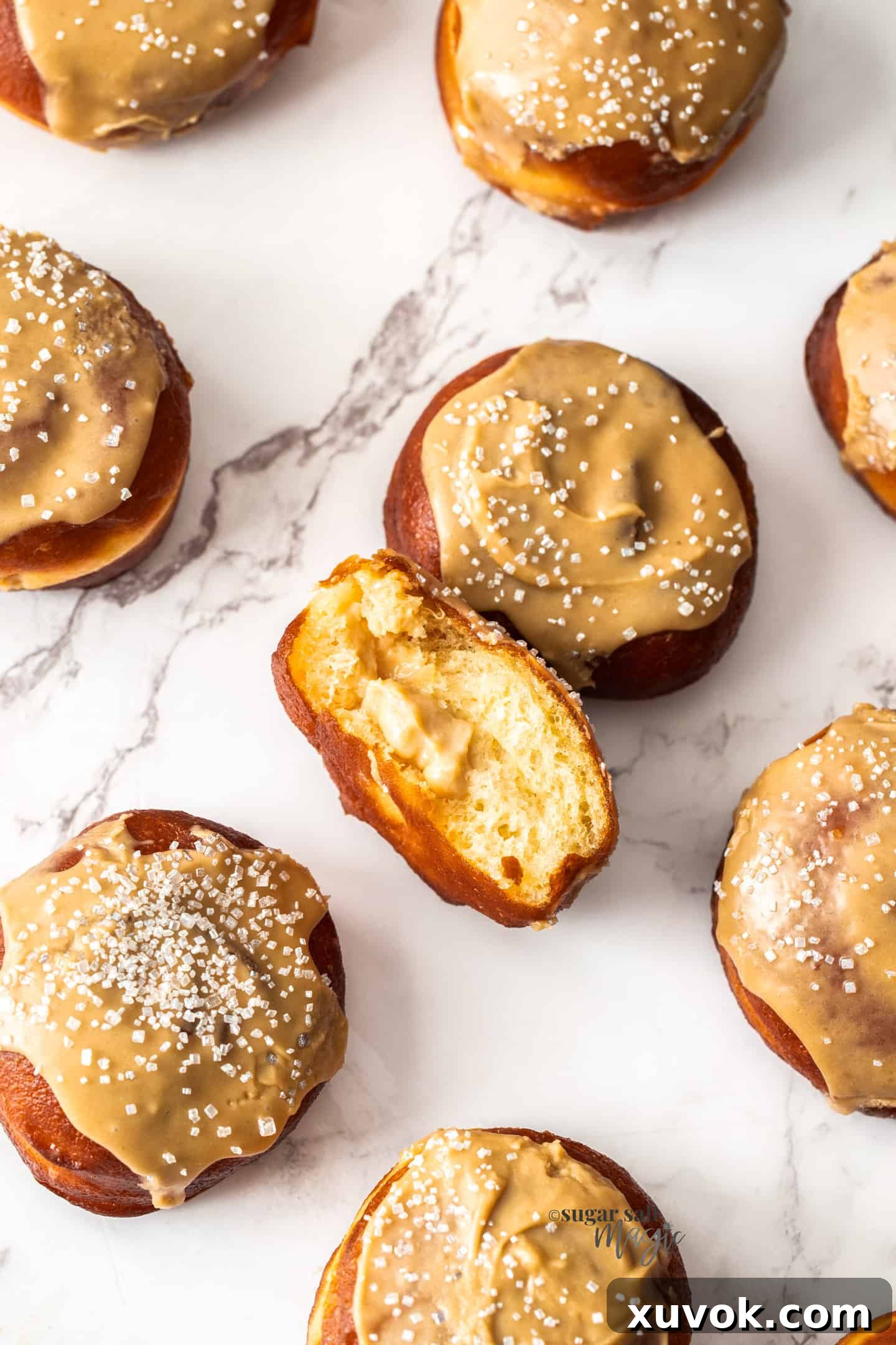 Top down view of fluffy caramel doughnuts on a marble benchtop, showcasing their golden brown exterior and glossy caramel icing.