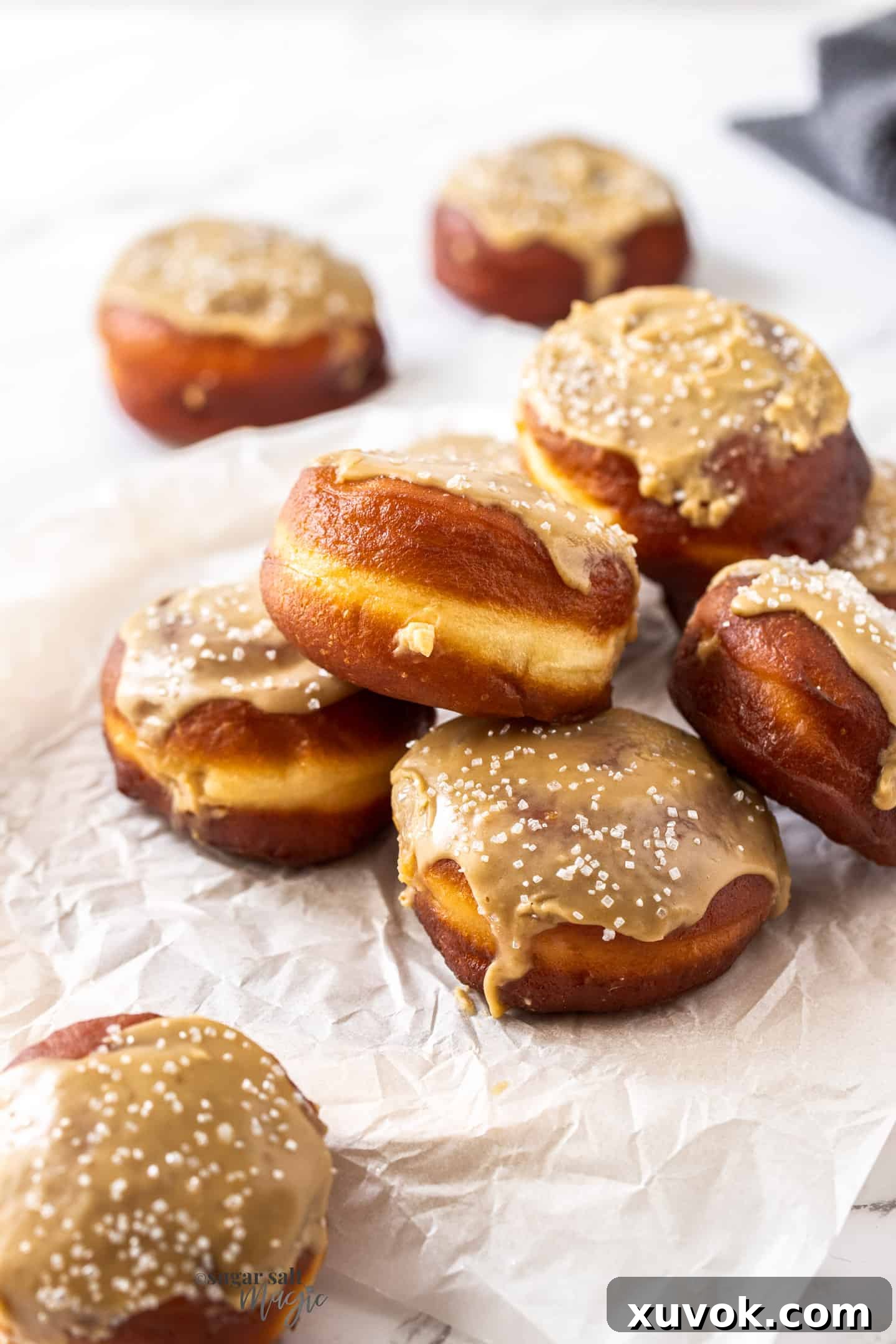A delightful pile of fluffy caramel doughnuts, beautifully topped with glossy caramel icing, arranged on a sheet of baking paper.