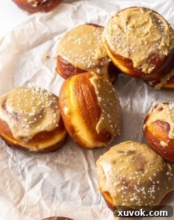 Top down view of a batch of fluffy caramel doughnuts on a sheet of baking paper, ready to be filled and iced.