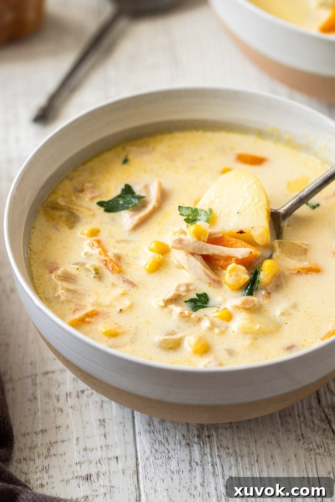 A close-up of a bowl of creamy turkey corn chowder with a spoon, showing its rich texture and chunks of turkey, corn, and potatoes.