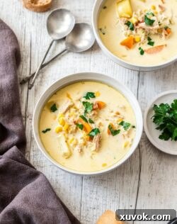 A bowl of creamy turkey corn chowder, garnished with fresh herbs, with a blurred second bowl in the background.