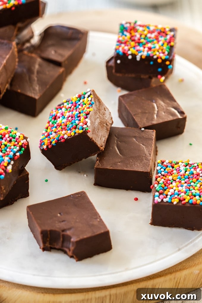 A batch of dark chocolate fudge pieces on a white marble platter, some adorned with colorful sprinkles, showcasing the rich texture of easy homemade fudge.