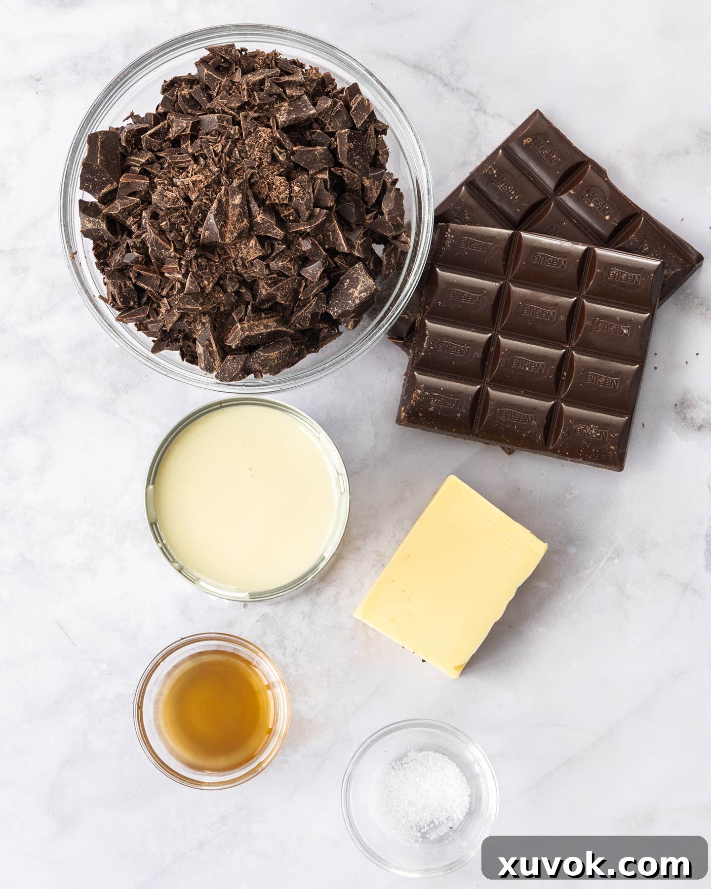 A curated selection of ingredients for making decadent dark chocolate fudge displayed on a pristine marble surface.