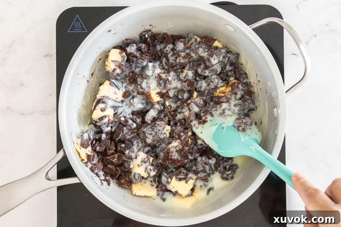Fudge ingredients — chopped dark chocolate, condensed milk, and butter — gently melting together in a saucepan over low heat.