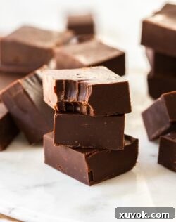 A stack of dark chocolate fudge pieces on a white marble platter. The top one has a bite taken out of it