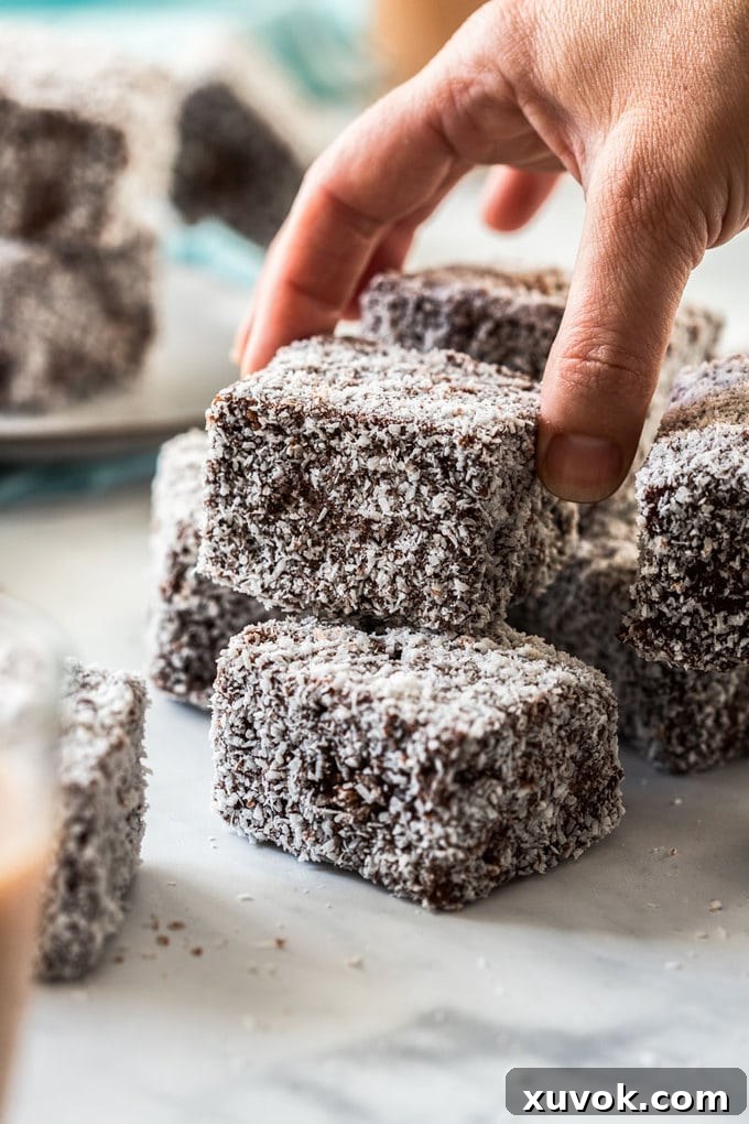 A hand picking up a lamington from a pile.