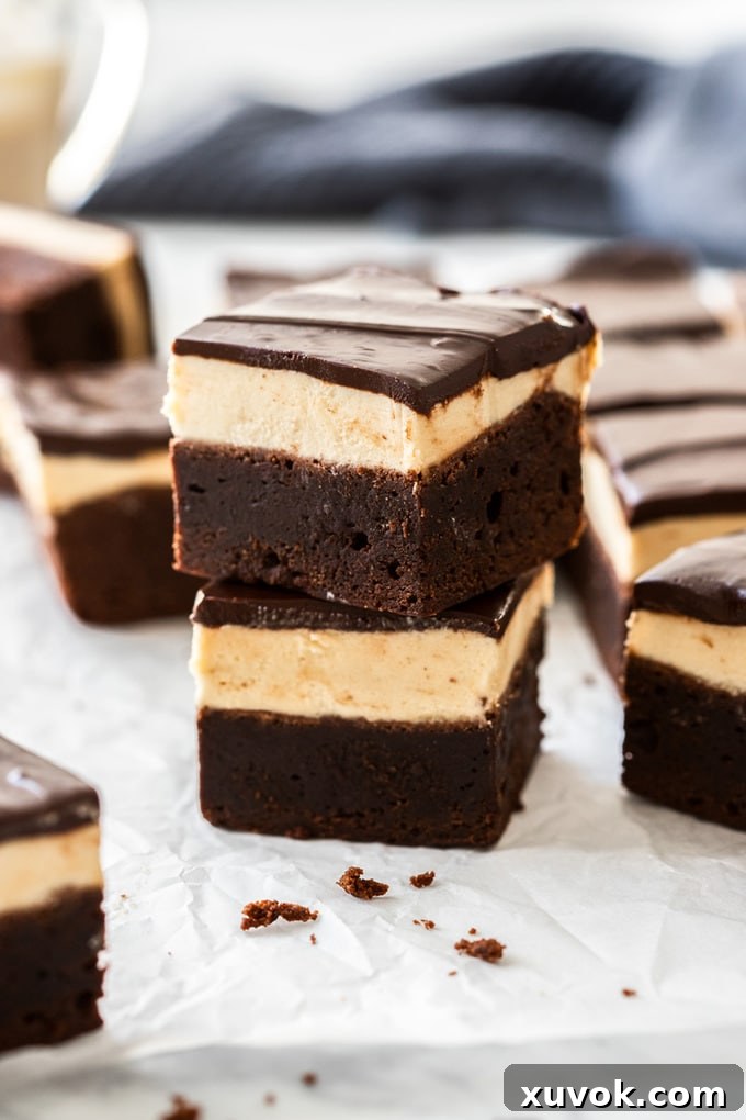 A stack of two Baileys brownies on a sheet of baking paper with more brownies around them, showcasing the rich layers of chocolate brownie, creamy Baileys buttercream, and smooth chocolate ganache.