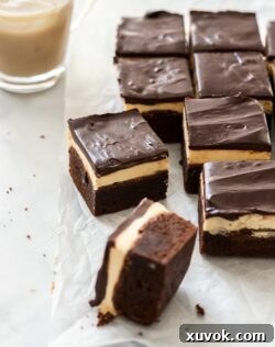 A batch of Baileys brownies on a sheet of baking paper with a glass of Baileys on ice in the background, ready to be enjoyed.