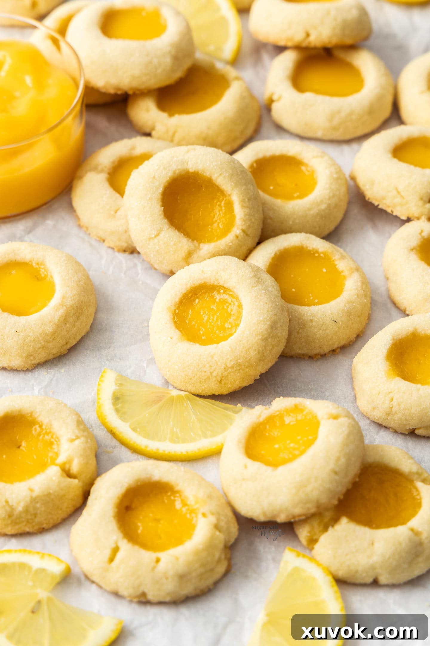 A large batch of golden-brown lemon curd thumbprint cookies arranged neatly on a sheet of baking paper, showcasing their perfect round shapes and vibrant yellow lemon centers.