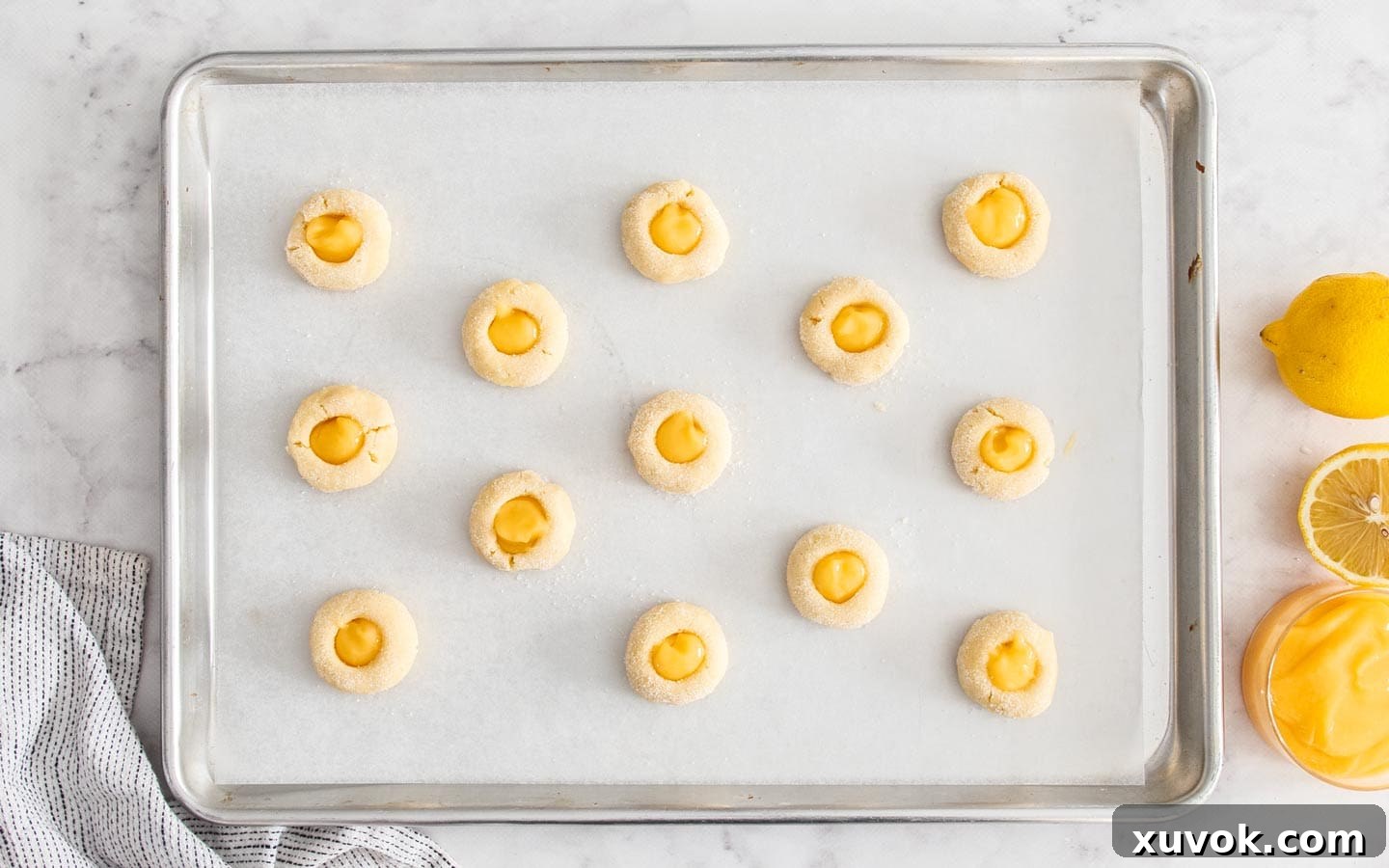 A baking tray filled with perfectly shaped lemon curd cookies, each indent brimming with bright yellow lemon curd, beautifully arranged and ready to be baked to golden perfection.