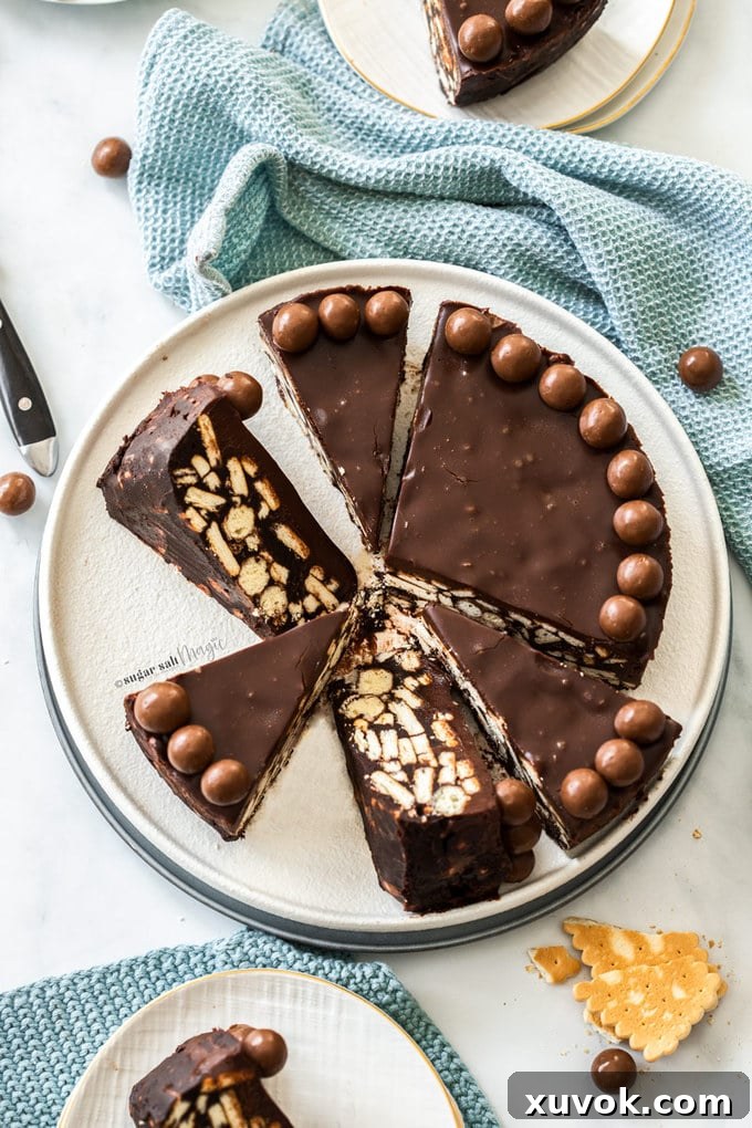 A large, beautifully sliced no-bake chocolate fridge cake, adorned with Maltesers on top, displayed on a clean white serving plate, ready to be portioned.