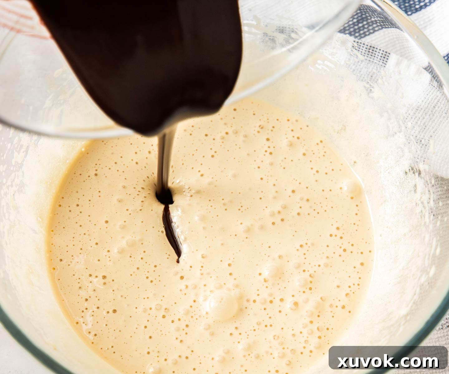 Melted chocolate and butter mixture being poured into a bowl of light, fluffy whipped eggs and sugar.