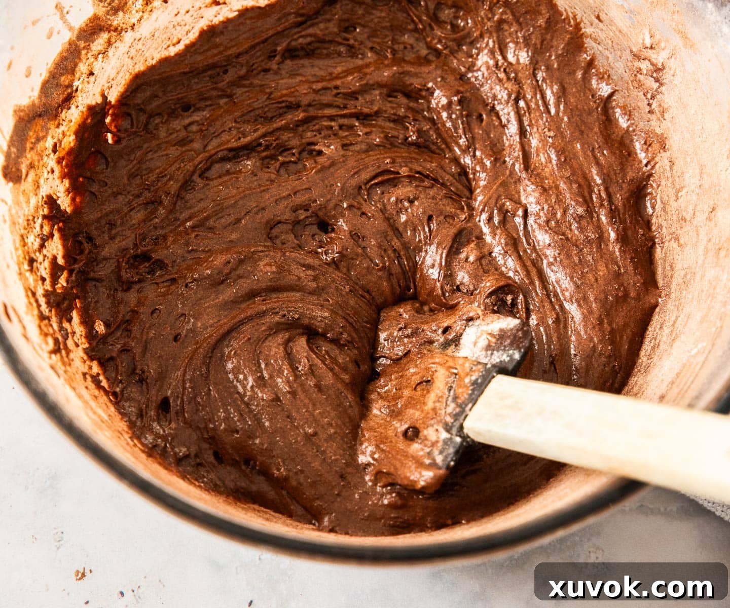 The dark, rich chocolate brownie batter in a mixing bowl with a silicone spatula sticking out, ready for baking.