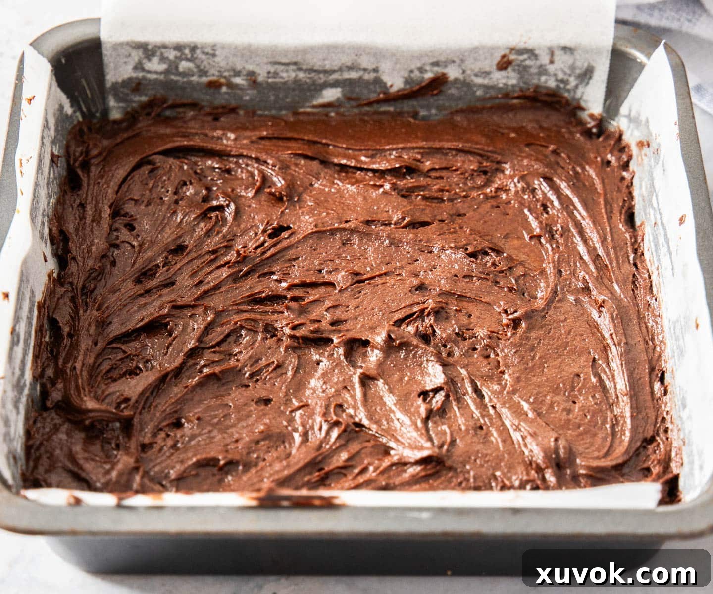 The layered brownie batter, with caramel visible underneath, spread out evenly in the baking pan, ready to bake.