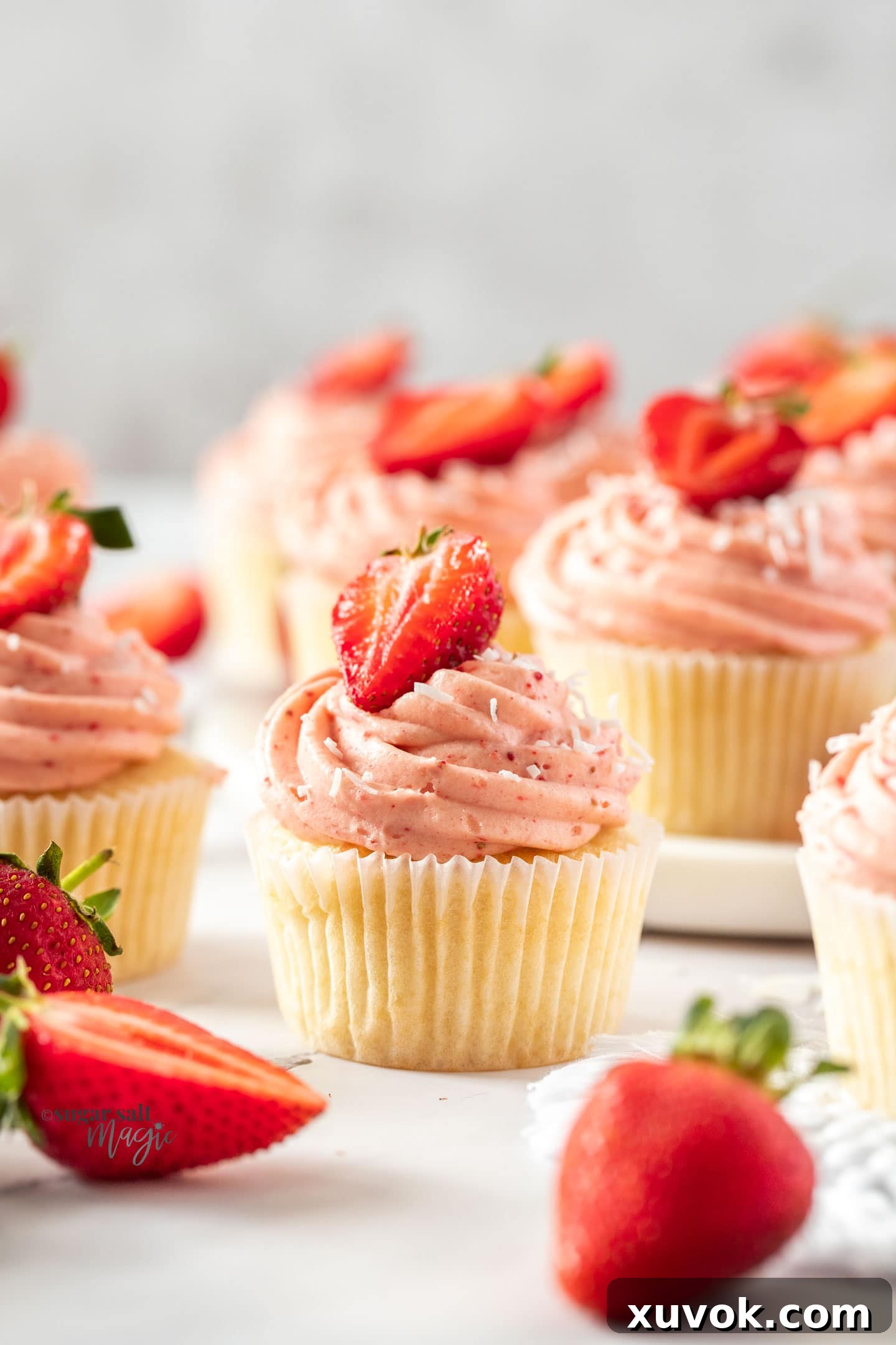 Closeup of a strawberry cupcake with pink cream cheese frosting and a fresh strawberry on top