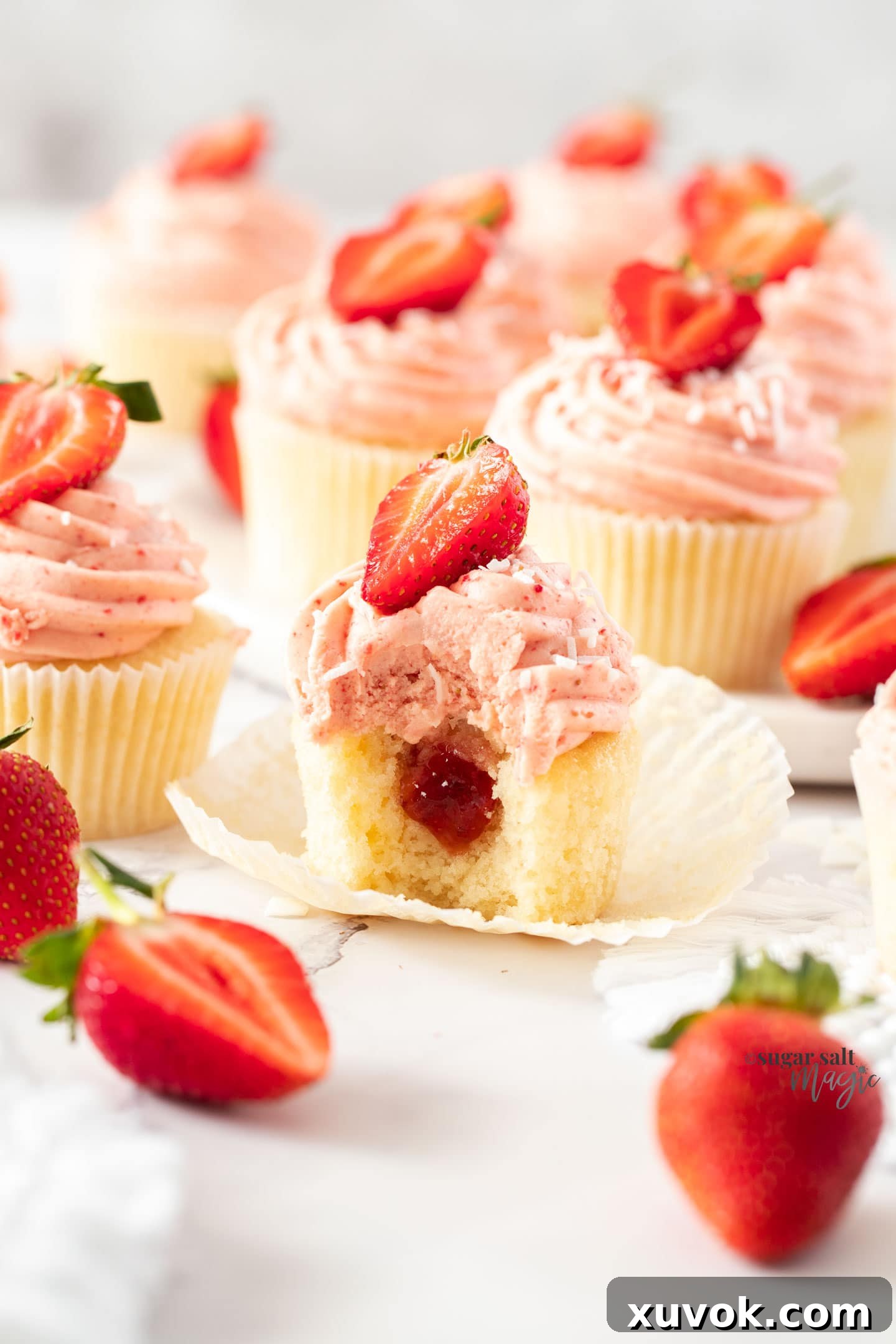 Close up of the inside of a white cupcake with pink frosting and jam in the middle