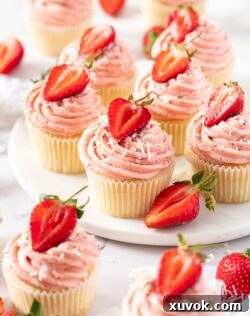 6 strawberry cupcakes on a white platter with a few more in front
