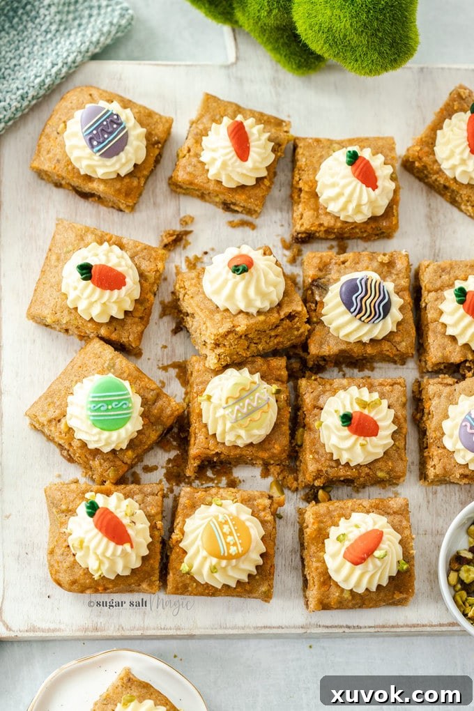 A birdseye view of 12 carrot cake bars topped with cream cheese frosting and royal icing easter decorations