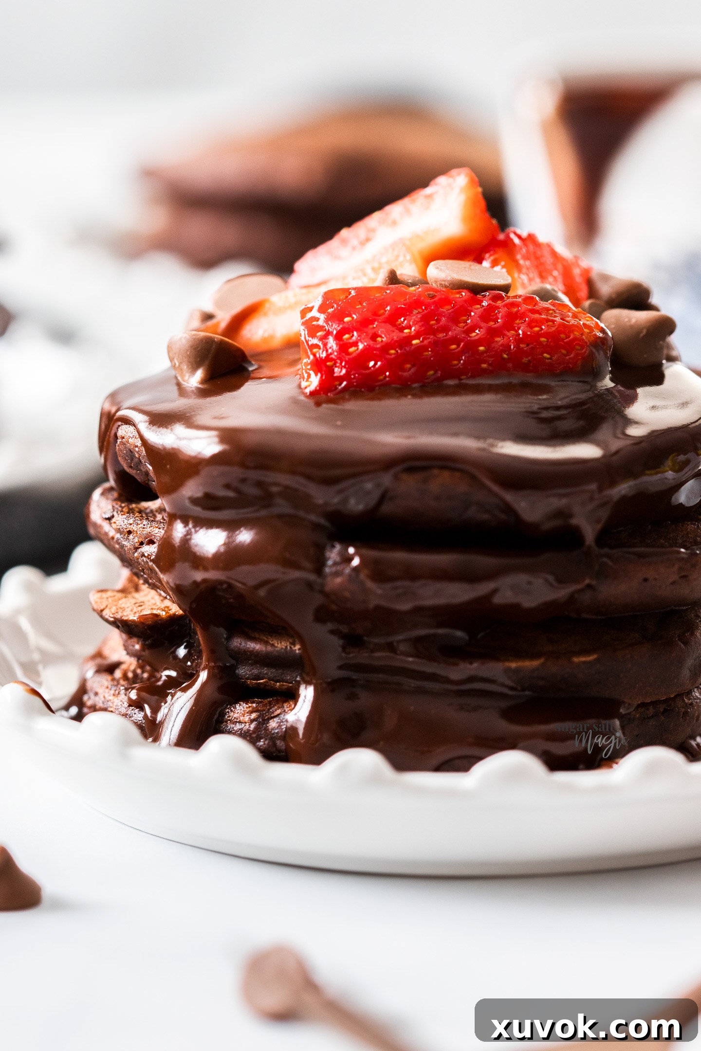 Closeup of a stack of chocolate pancakes with rich chocolate sauce running down the side, adorned with fresh raspberries.