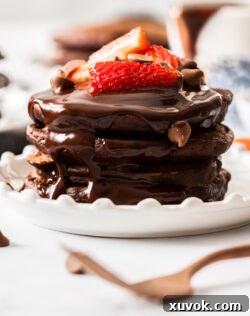 A stack of chocolate pancakes topped with strawberries and a dusting of powdered sugar.