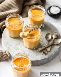 Small glass jars on a grey platter, filled with caramel custard. One has a spoon sitting on top, indicating it's ready to eat.