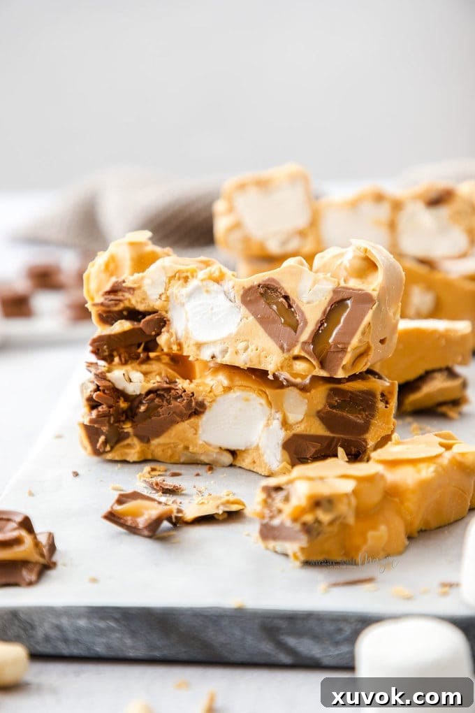 Two generous pieces of homemade Caramel White Chocolate Rocky Road Slice stacked, with more slices artfully arranged around them on a pristine white surface.