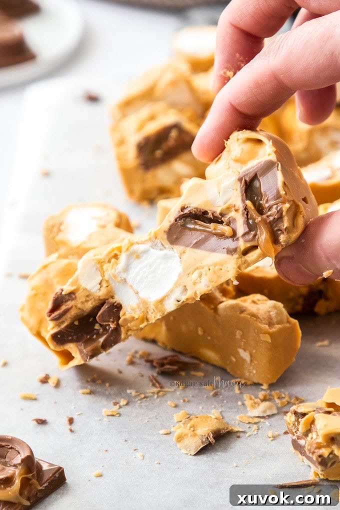 A hand gracefully holds a piece of Caramel White Chocolate Rocky Road, highlighting its irresistible texture and the rich blend of ingredients.