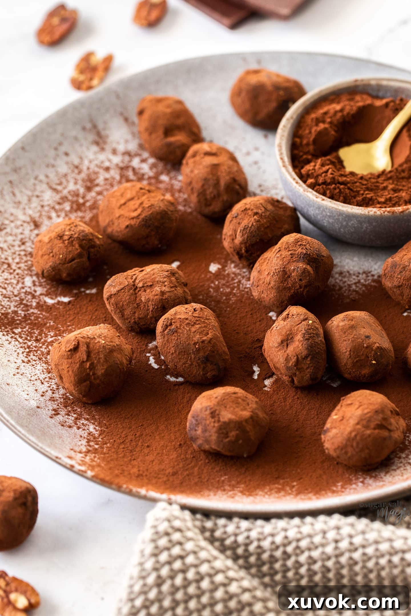 A generous plate of homemade Toffee Pecan Chocolate Truffles, with a small bowl of rich cocoa powder beside them, ready for rolling.