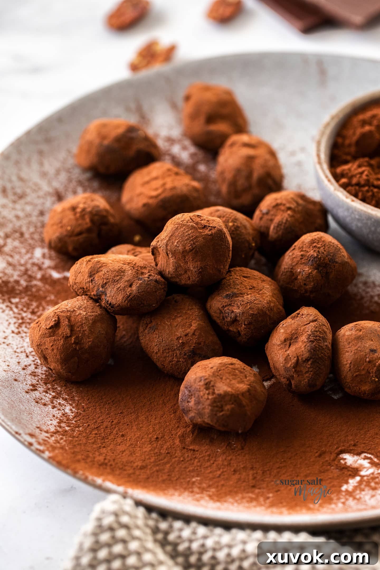 A beautifully arranged pile of glistening Toffee Pecan Chocolate Truffles on a sophisticated grey plate, highlighting their rich color and inviting texture.