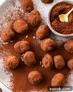 A batch of chocolate truffles on a plate with a small bowl of cocoa