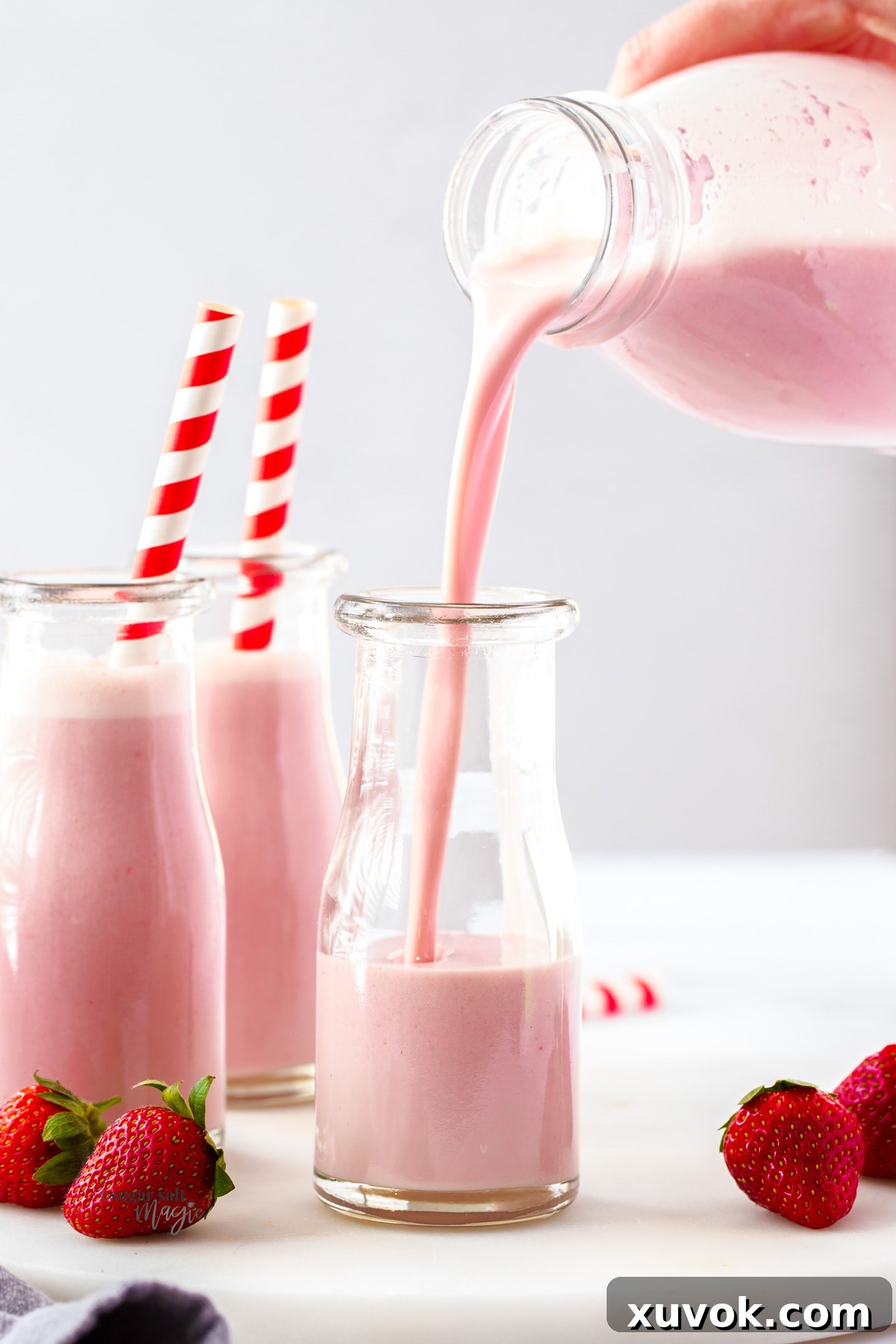 Fresh homemade strawberry milk being poured into a miniature milk bottle, highlighting its vibrant color and smooth texture.