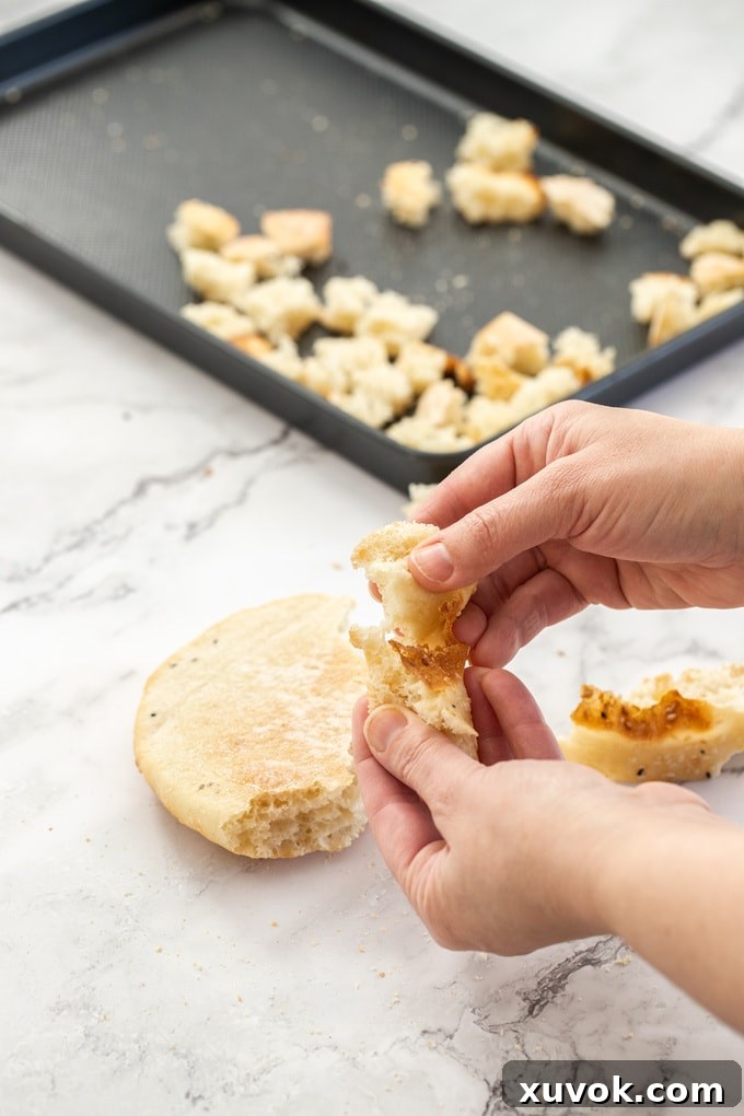 Hands tearing apart bread into small chunks.