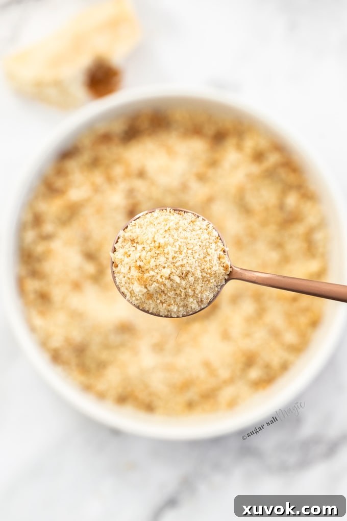 Close up of breadcrumbs on a spoon above a bowl filled with breadcrumbs.
